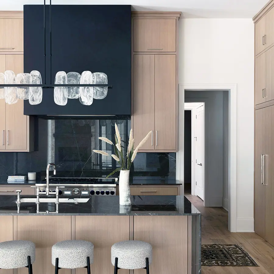 Kitchen with light wood cabinets, black range hood and dark marble backsplash