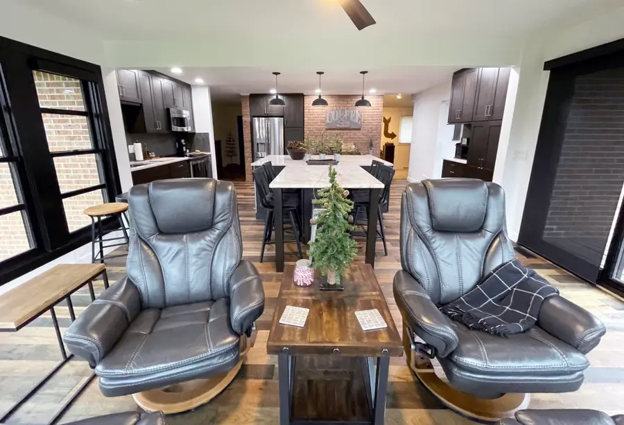 Open kitchen with dark cabinets and marble island seen past two leather recliners