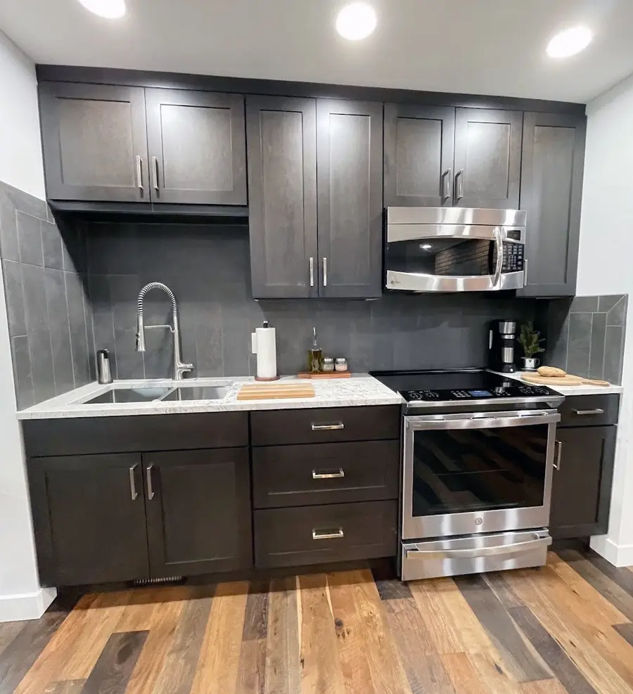 Compact kitchen wall with charcoal cabinets, gray tile, stainless range and microwave