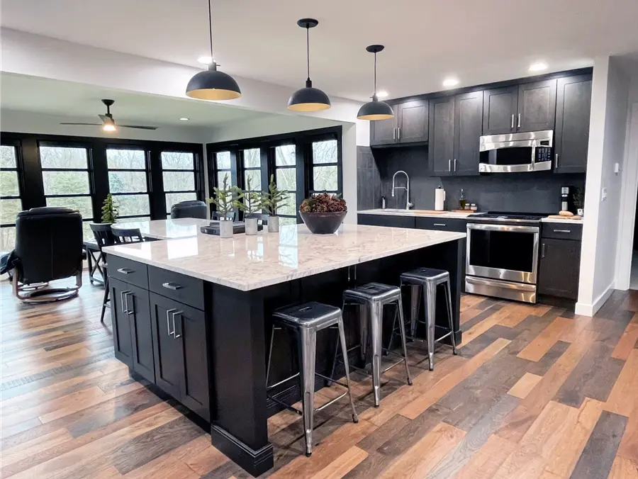Kitchen with black cabinets, granite island, metal stools and dome pendants