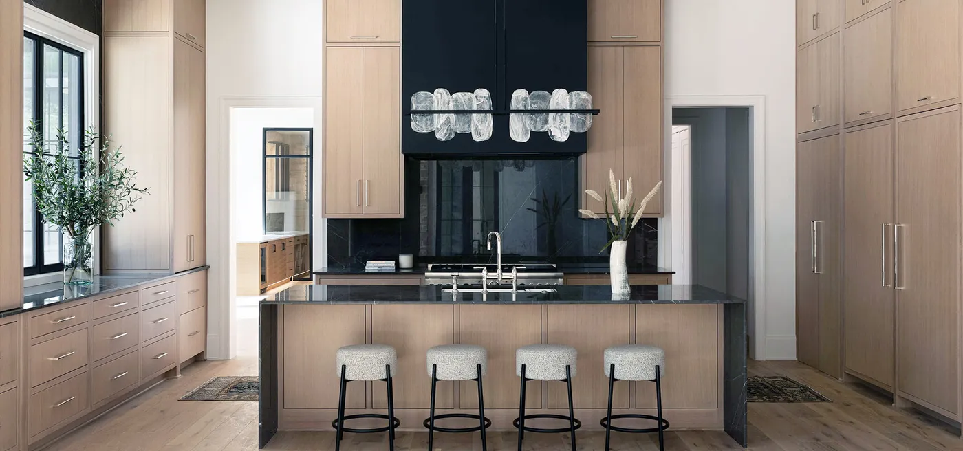 Modern kitchen with light wood cabinets, dark island, stools and statement chandelier
