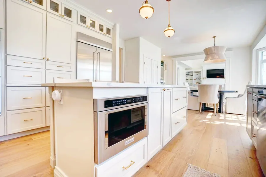 White kitchen island with drawer microwave, brass pulls and pendant lights, dining area beyond