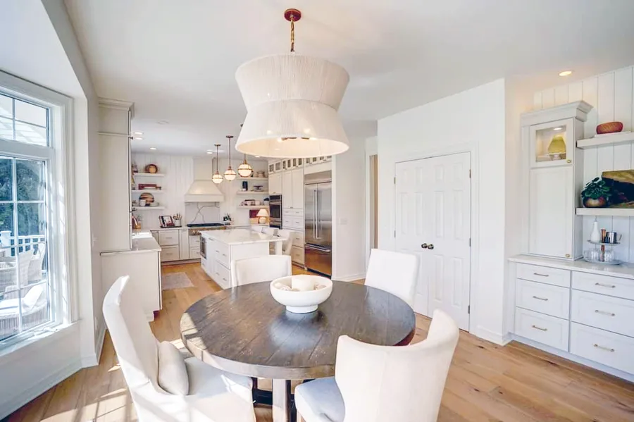 Round dining table under a drum pendant with a white kitchen and built-in hutch beyond