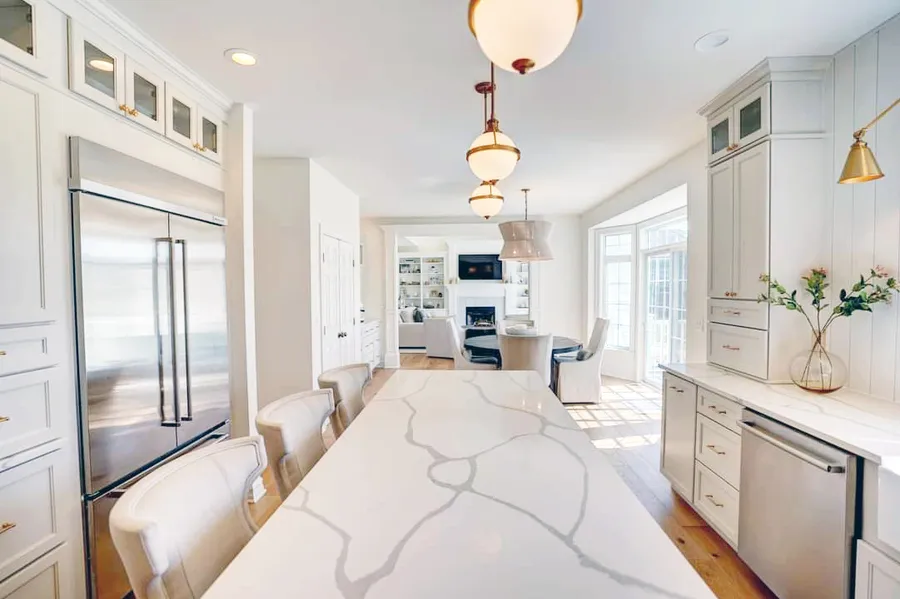 Long marble-look island with upholstered stools in a white kitchen opening to living room