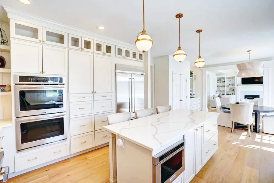 White kitchen with marble-look island, double wall ovens, globe pendants and wood floors