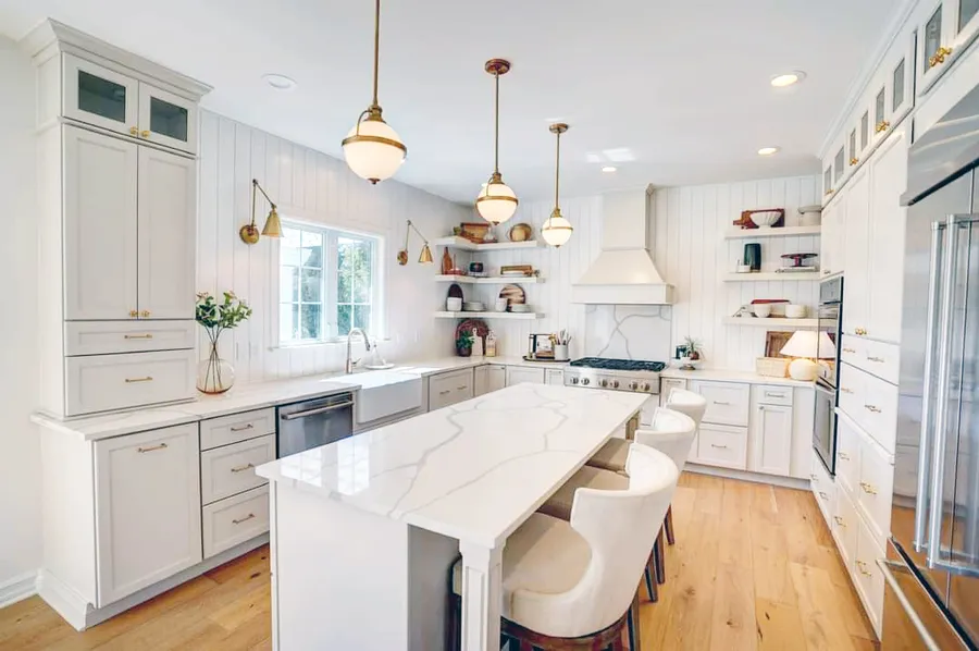 White kitchen with vertical shiplap walls, marble-look island and brass globe pendants