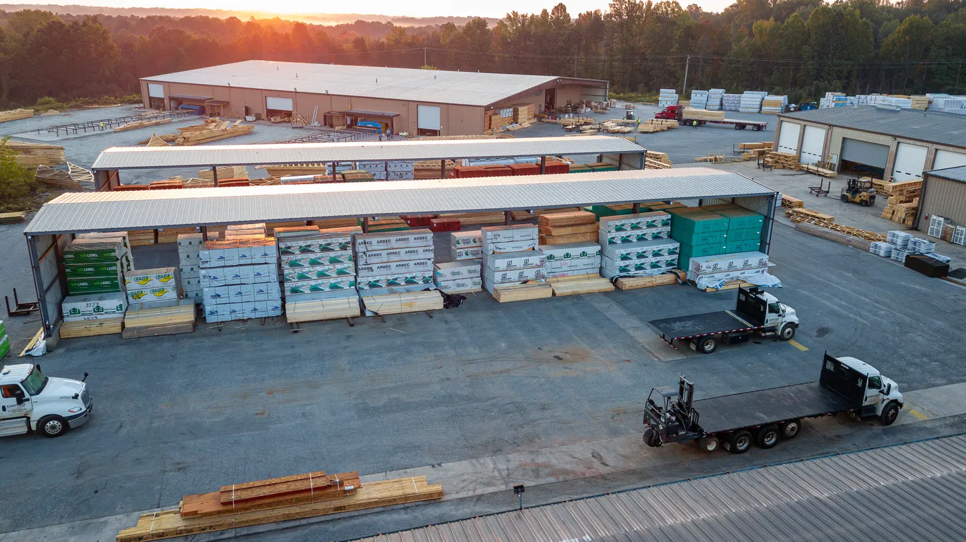 Aerial view of a lumber yard with covered material storage and flatbed trucks at sunset