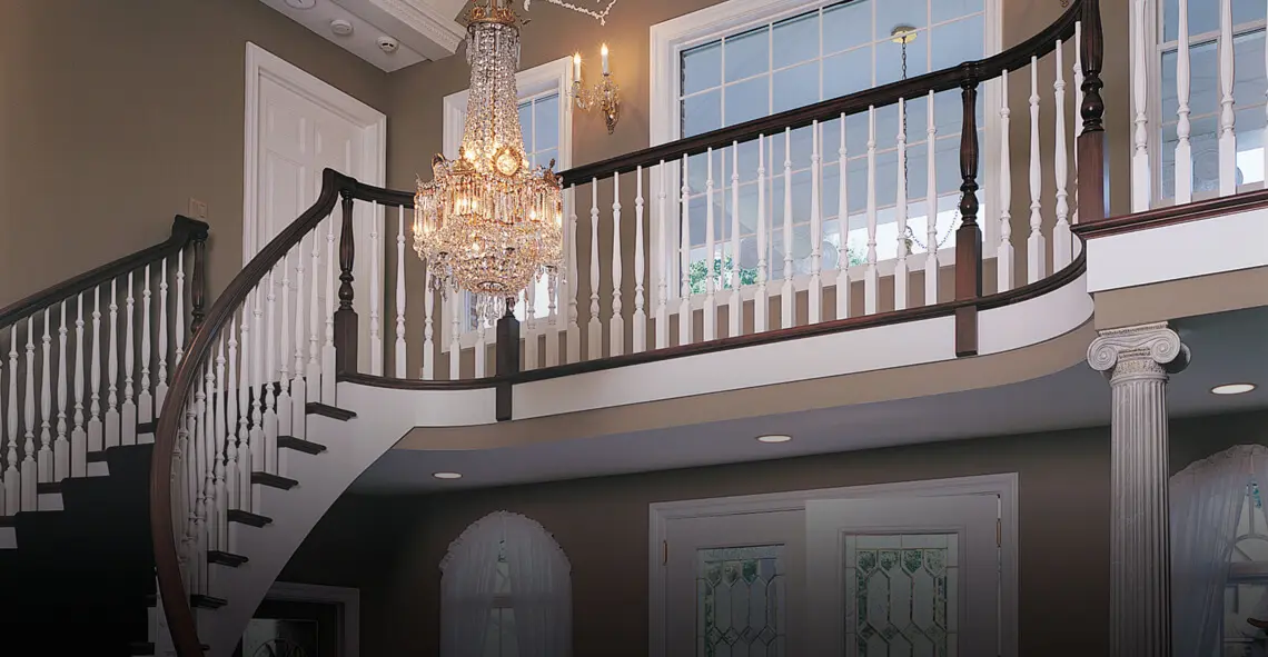 Two-story foyer with a curved staircase, white balusters, dark handrail and crystal chandelier