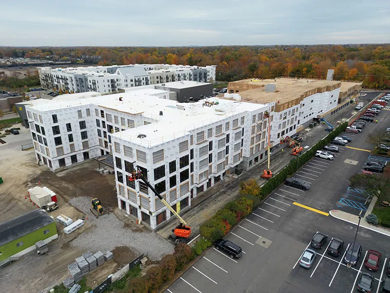 Aerial view of a multi-story apartment building wrapped in house wrap with lifts on site