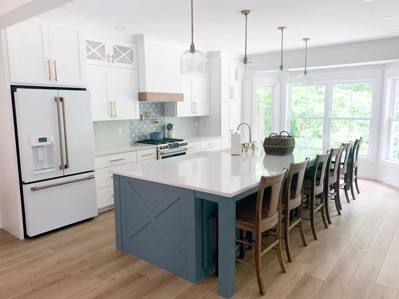 White kitchen with blue X-panel island, wood chairs, white refrigerator and brass pendants