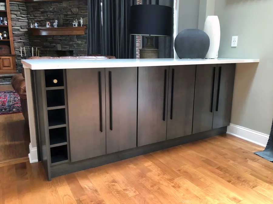 Gray-brown peninsula cabinets with wine cubbies, long black pulls and white countertop