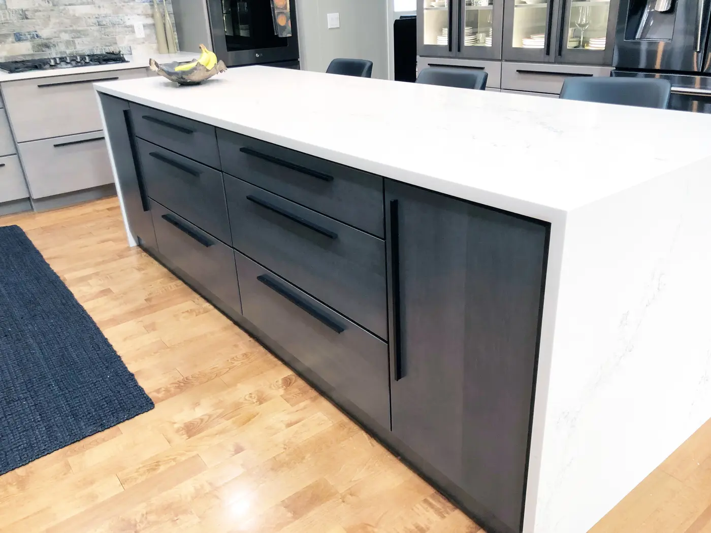 Gray island with long black pulls and white waterfall countertop