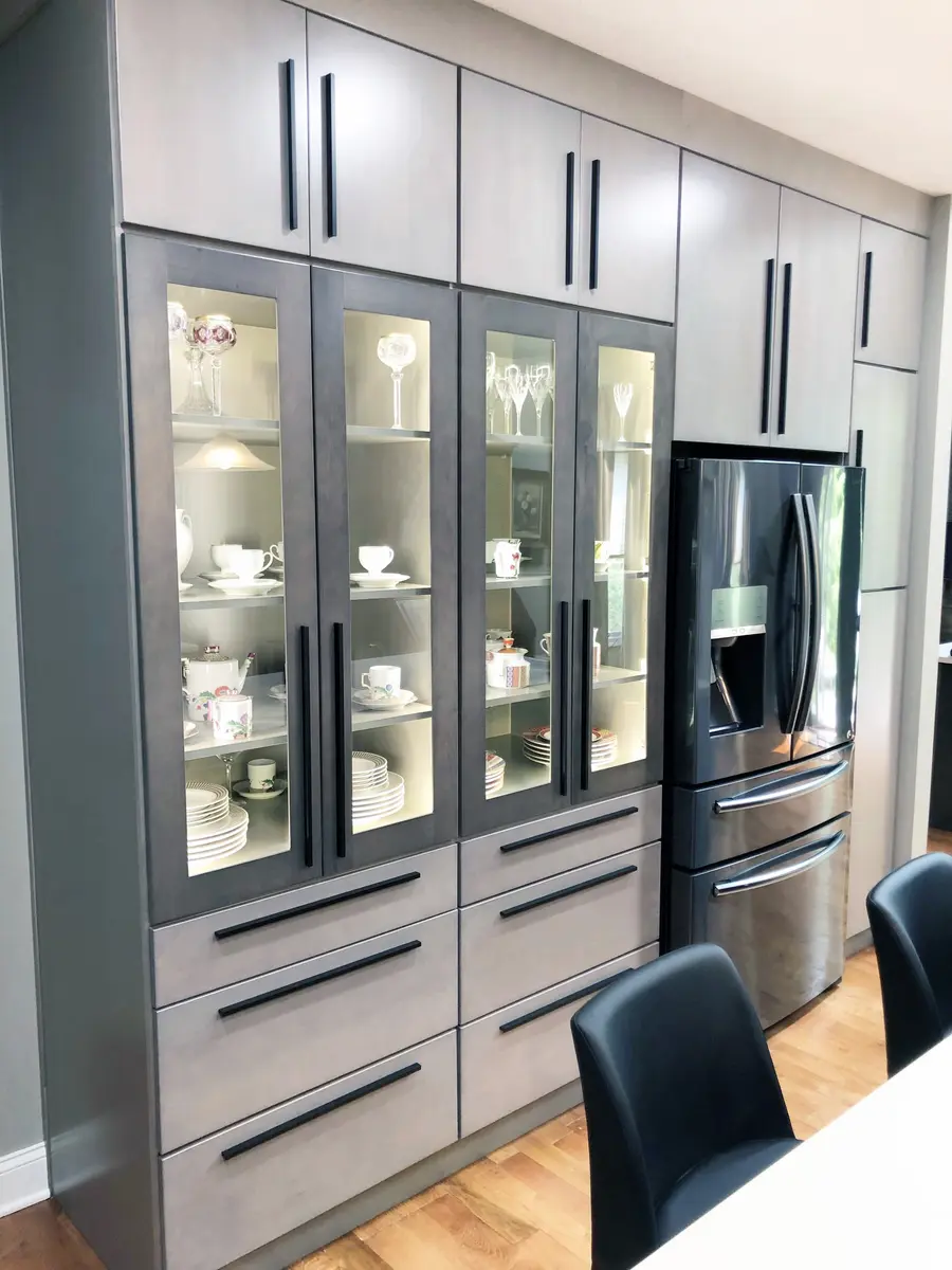 Wall of gray glass-front display cabinets with long black pulls beside a dark refrigerator