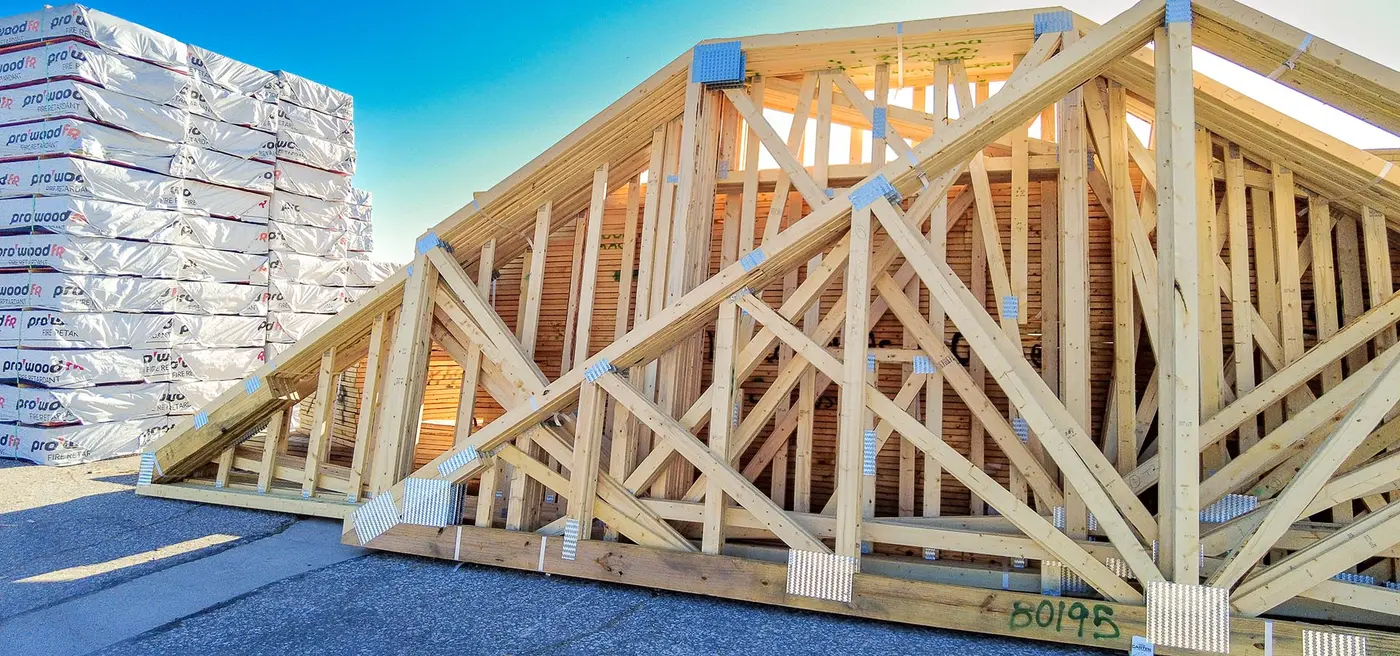 Wood roof trusses with metal connector plates stacked beside wrapped lumber in a yard