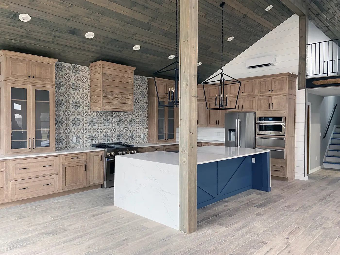 Rustic kitchen with wood cabinets, patterned tile backsplash, waterfall island and lantern pendants