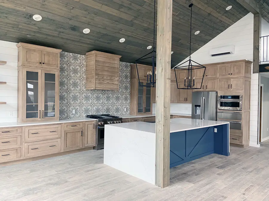 Natural wood cabinets, patterned tile wall, and blue island with waterfall stone top