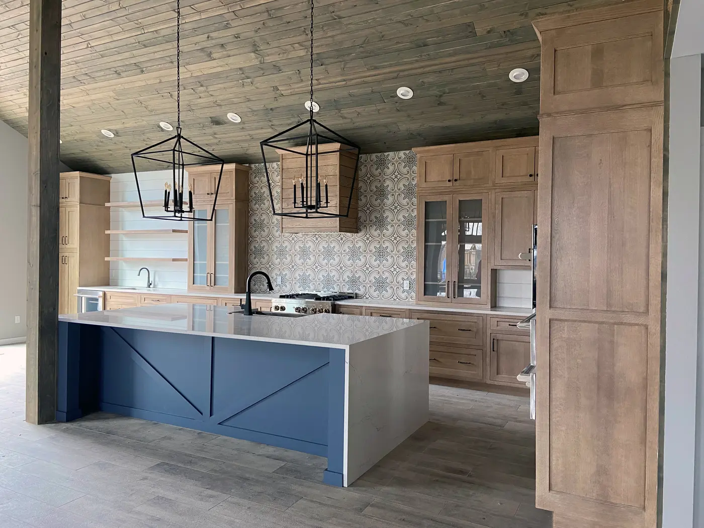 Blue X-panel island with waterfall top beside tall natural wood cabinets and patterned tile