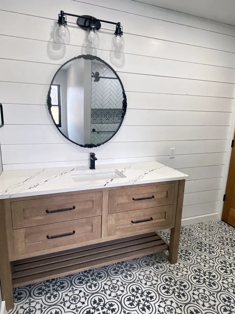 Bathroom vanity in weathered wood with stone top, round mirror, and patterned floor tile
