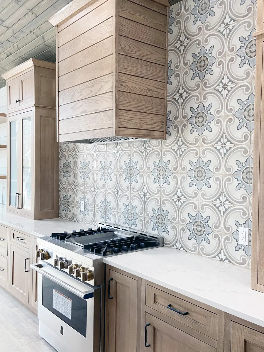 Wood-clad range hood over a stainless gas range with blue and gray patterned tile