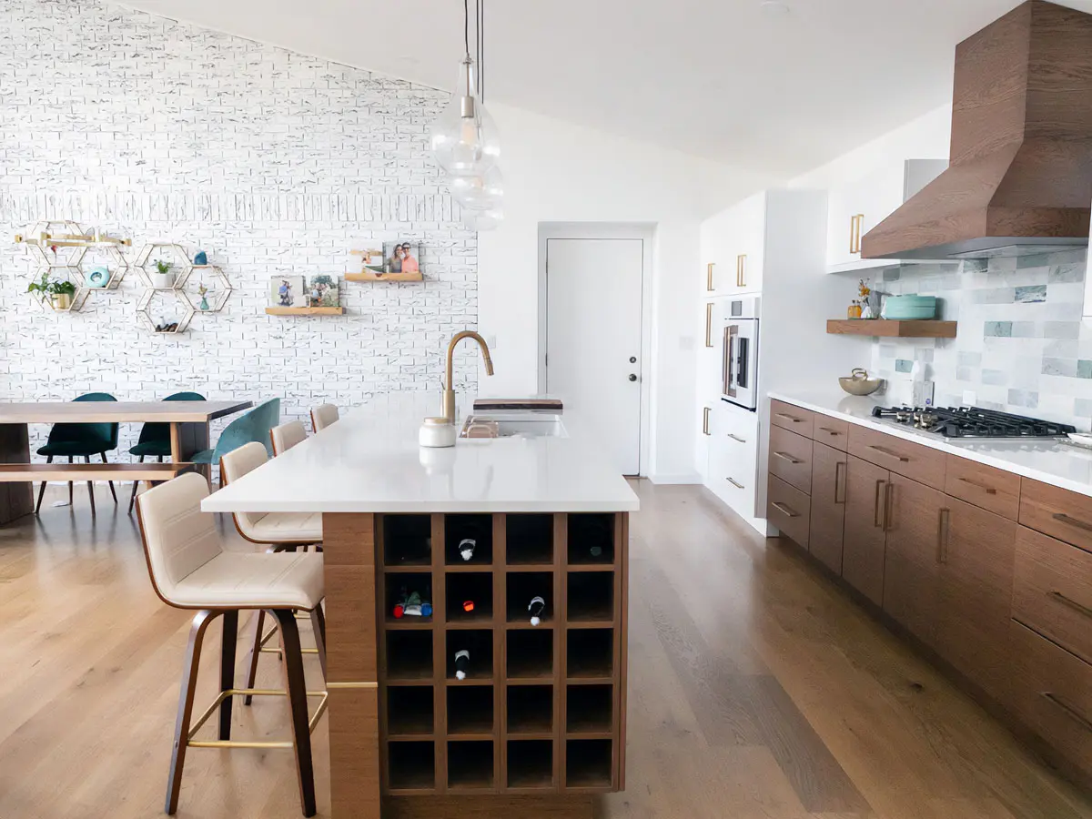 Open kitchen with white island, built-in wine cubbies, wood lower cabinets and copper range hood